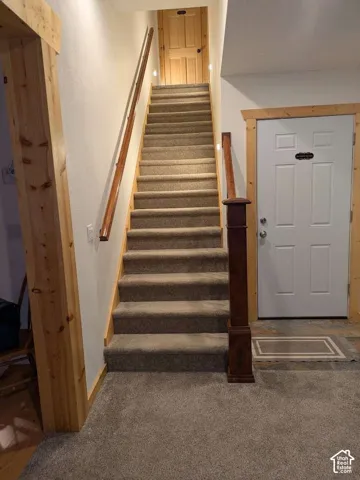 Carpeted staircase with wood handrail, wood newel post, and wood trim detailing