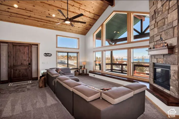 Vaulted wood-paneled ceiling, stone-clad fireplace with wood mantle, large floor-to-ceiling windows, and wood-framed entry door