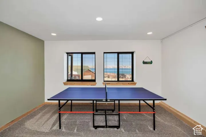 Recessed lighting illuminates a space featuring two windows with horizontal blinds, wood-finish window sills, and carpeting