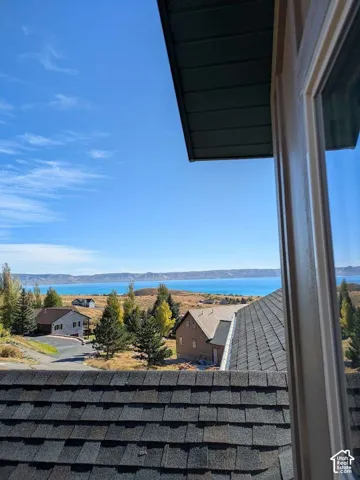 Expansive water scenery framed by a window, featuring distant mountains and a textured shingle roof
