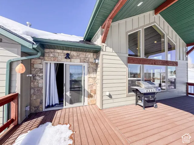 Expansive outdoor deck with wood-finish decking, stone facade, sliding glass door, and large windows