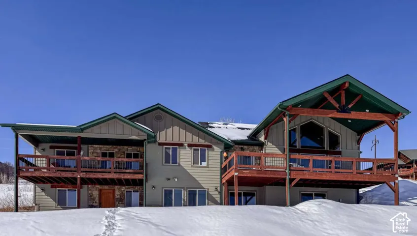 Expansive rear exterior featuring multiple decks, a covered patio, stone accents, broad windows, and a distinctive gable roofline