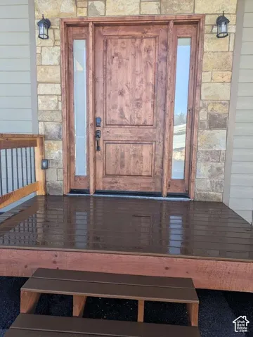 Wood-paneled entry door with sidelights, stone veneer facade, and matching exterior sconces