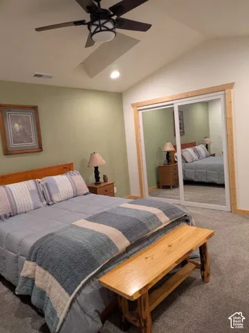Sliding mirrored closet doors, carpet flooring, a ceiling fan with integrated lighting, and a vaulted ceiling