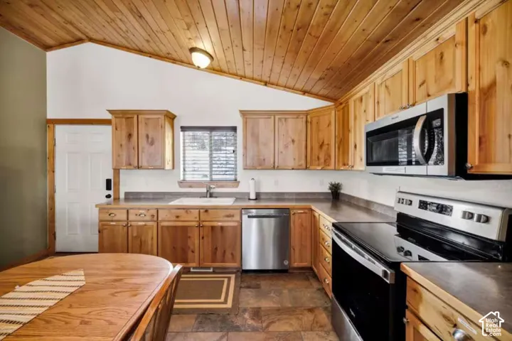 Angled wood-paneled ceiling, wood-finish cabinetry, stainless steel appliances, solid surface countertops, and slate-style flooring