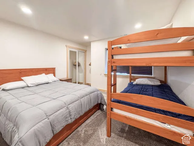 Recessed lighting illuminates this room featuring carpeted flooring, a window with blinds, and a built-in closet with sliding doors