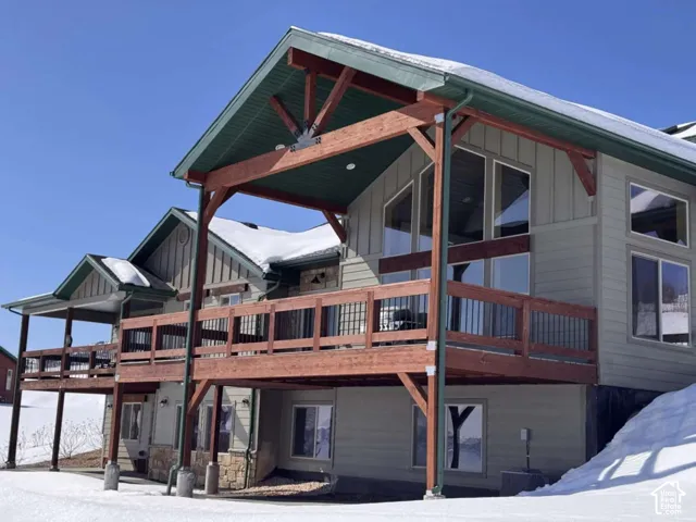 Multi-level exterior featuring a covered deck, substantial wood framing, large windows, and a stone foundation