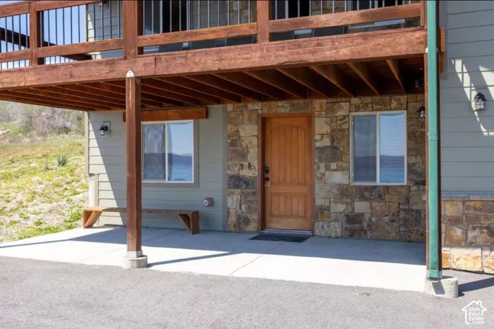 Stone veneer and siding facade with a wooden entry door, ground-level patio, and an overhead wood-finish deck