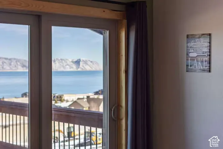 Sliding glass doors opening to an exterior balcony with a railing, offering a waterfront and mountain backdrop