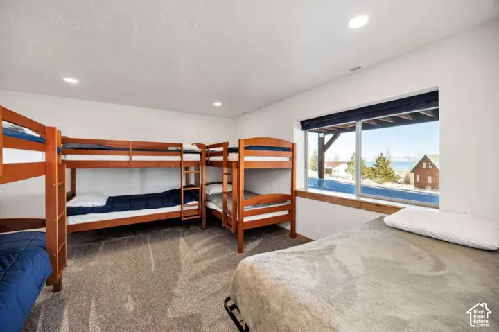 Spacious room featuring multiple wooden bunk beds, recessed lighting, carpeted flooring, and a large window overlooking a distant body of water