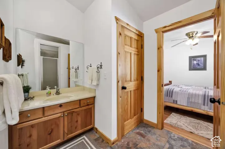 Wood-finish vanity with dual sinks, a large wall-mounted mirror, and dark-toned floor tiles