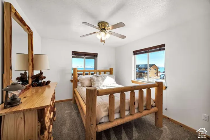 Ceiling fan with integrated lighting, two windows with blinds, wood-frame windows, and carpeted flooring