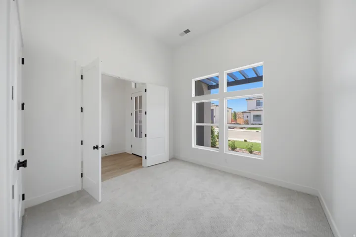 Vaulted ceilings, large windows, light gray carpeting, white walls, and French doors with matte black hardware