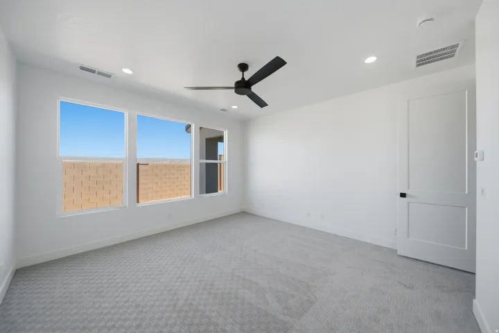 White walls, light-toned patterned carpeting, three large windows, a black ceiling fan, and recessed lighting fixtures