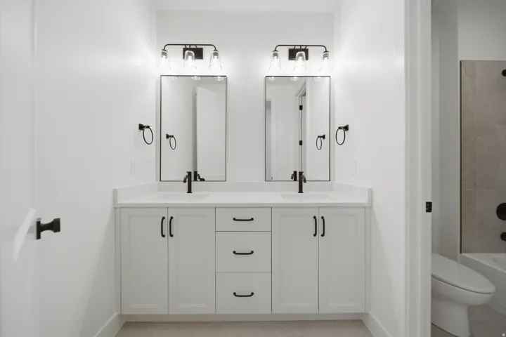 Dual vanity with white cabinetry, matte black fixtures, rectangular undermount sinks, and framed mirrors