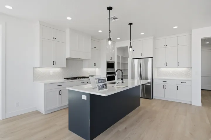 Kitchen featuring a central island with countertop, white cabinetry with dark hardware, herringbone tile backsplash, and stainless steel appliances