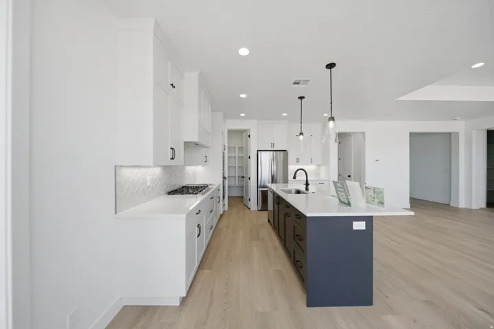Modern kitchen featuring white shaker cabinetry, white countertops, wood-finish flooring, a two-toned island, and pendant lighting