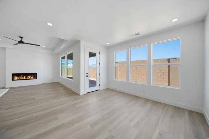 Spacious living area featuring wood-finish flooring, a linear electric fireplace, multiple windows, and a glass-paneled exterior door
