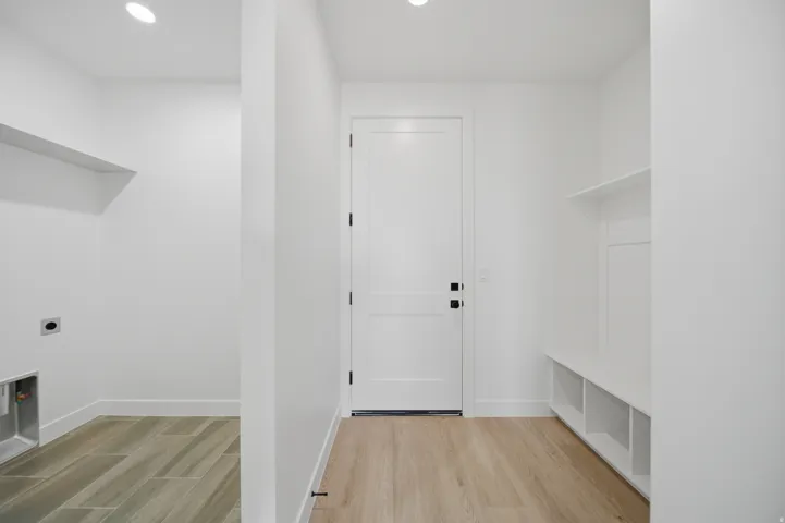 Recessed lighting, light wood-finish flooring, built-in storage bench, and a modern paneled door with matte black hardware