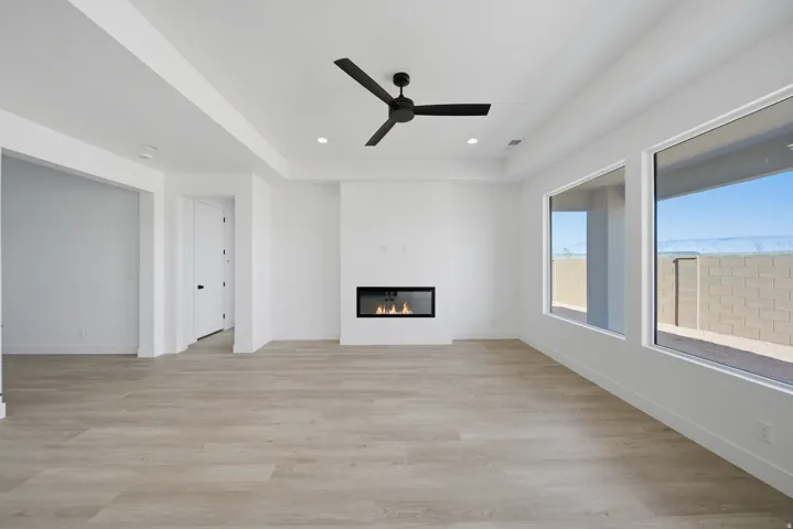 Spacious room featuring wood-finish flooring, a contemporary fireplace, large picture windows, a tray ceiling, and a modern ceiling fan