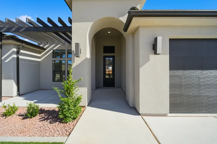 Stucco exterior with an arched entry, modern garage door, and a decorative pergola