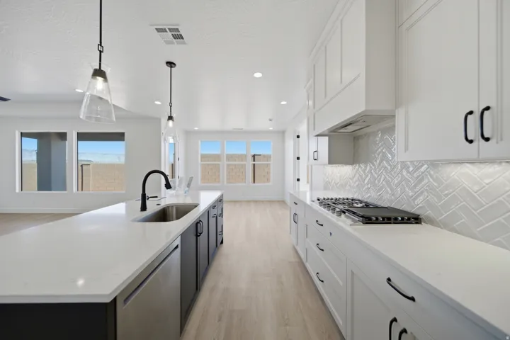 Kitchen featuring white cabinetry, a gas range, a herringbone tile backsplash, and an island with an undermount sink