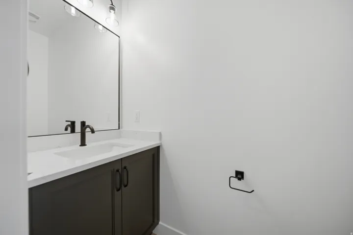 Modern vanity with a white countertop and integrated sink, dark cabinetry, and a black framed mirror