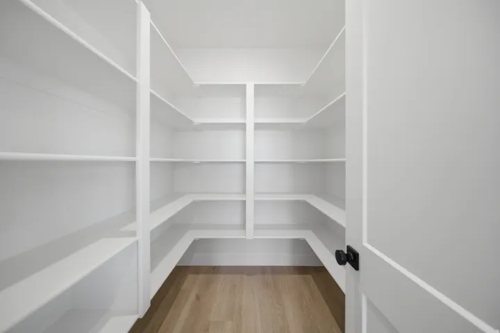 Walk-in pantry featuring expansive white shelving, L-shaped shelving configuration, and wood-finish flooring