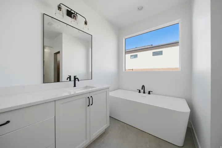 Freestanding soaking tub, white vanity with integrated sink, quartz countertop, matte black fixtures, and a large framed mirror