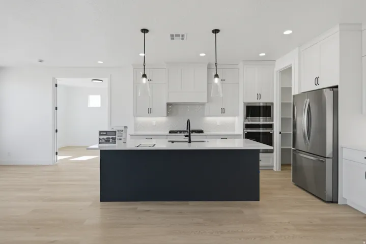Kitchen featuring white cabinetry, stainless steel appliances, a dark-toned island with a light-toned countertop, and wood-finish flooring