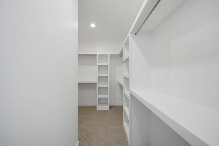 Built-in shelving, integrated hanging rods, recessed ceiling lighting, and carpet flooring