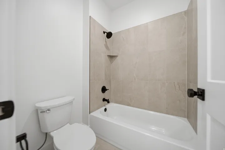 Bathtub with matte black fixtures, tiled surround, and integrated corner shelf