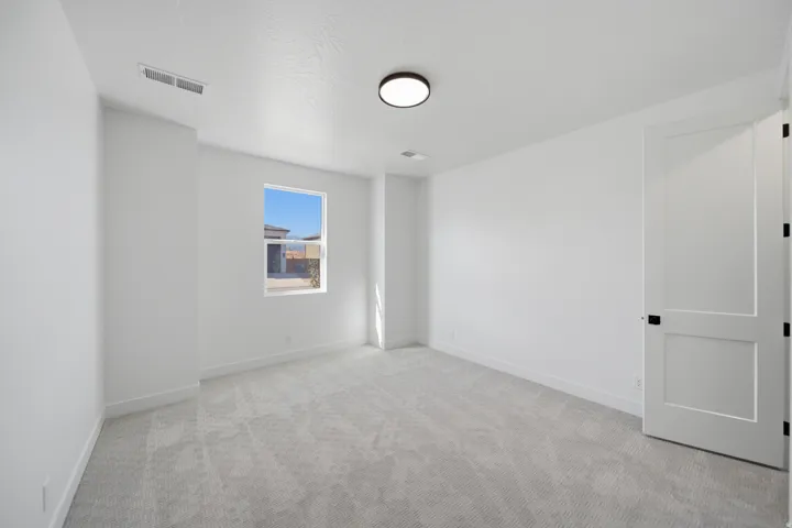 Neutral tone wall paint, light-colored carpeting, single window, flush-mount ceiling light fixture, and two-panel interior door with dark hardware
