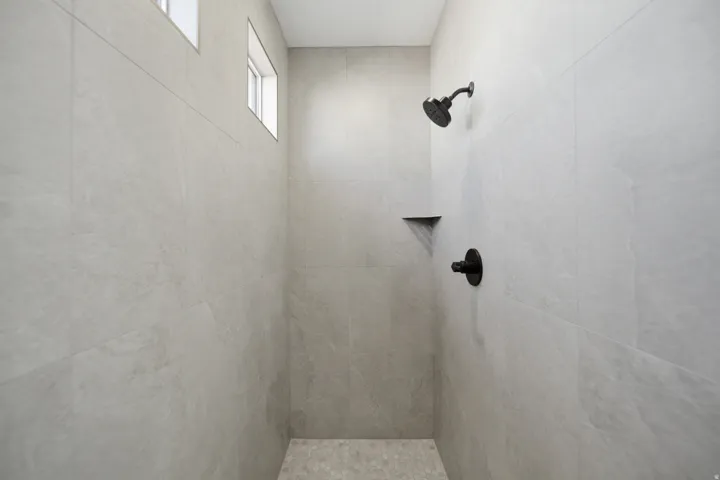 Shower enclosure featuring light-toned large format wall tiling, a built-in corner shelf, and matte black fixtures