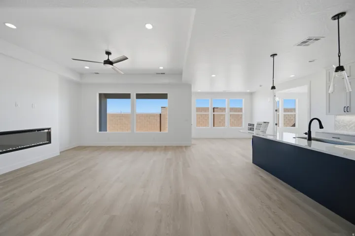 Open-concept living space with wood-finish flooring, a linear electric fireplace, recessed lighting, and an expansive island with a sink and pendant lighting