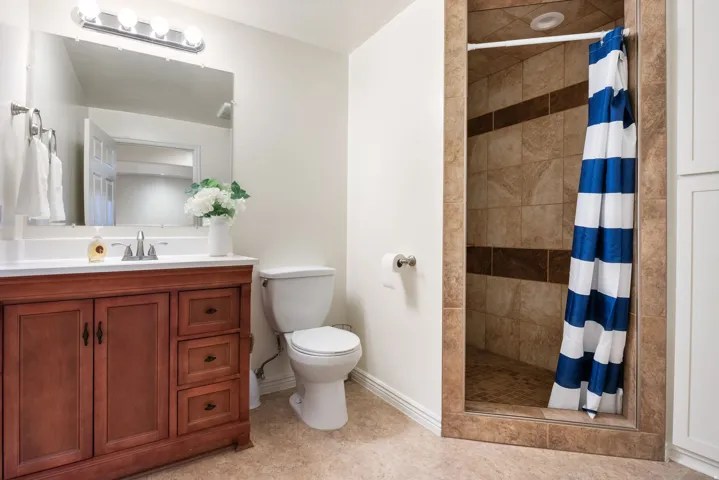 Wood vanity with a white countertop and integrated sink, chrome faucet, tiled shower with accent band, and vinyl flooring