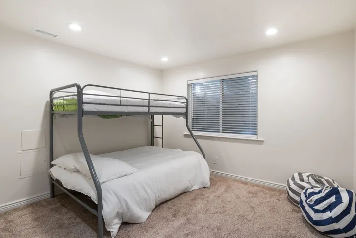 Recessed ceiling lighting, a window with blinds, and neutral-toned wall paint complement the carpeted flooring