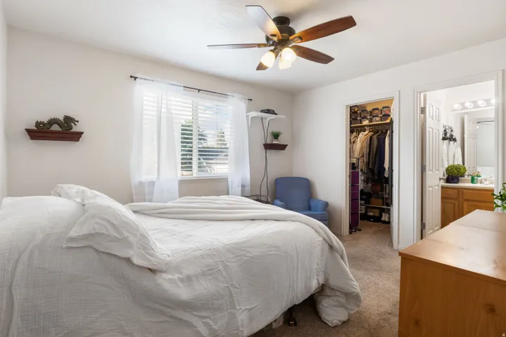 Ceiling fan with integrated lighting, window with horizontal blinds, built-in closet with shelving, wood-finish vanity with countertop, and wall-mounted light fixture in bathroom