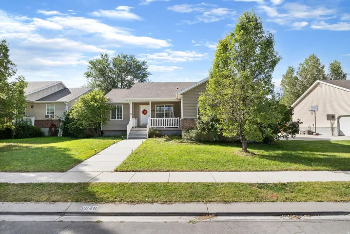 Exterior showcasing a covered porch, white railing, concrete steps, and a landscaped lawn