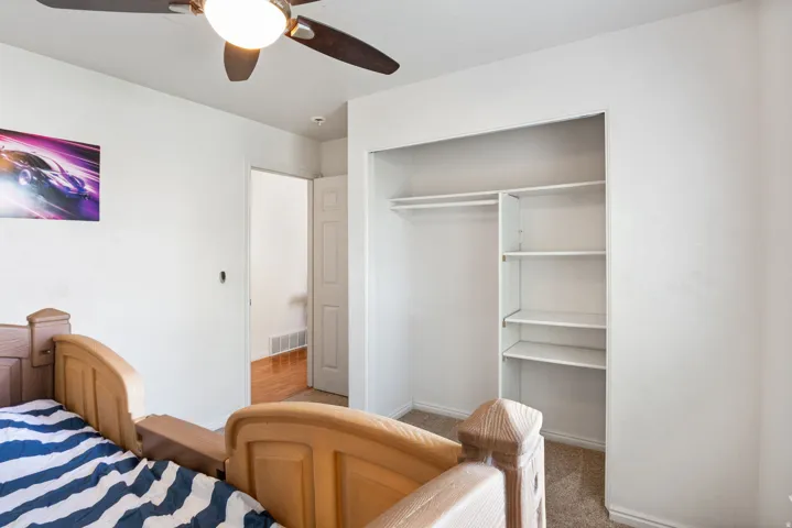 Ceiling fan with integrated lighting, open closet with hanging rod and shelving, light-toned carpet flooring, white painted walls, and an interior door