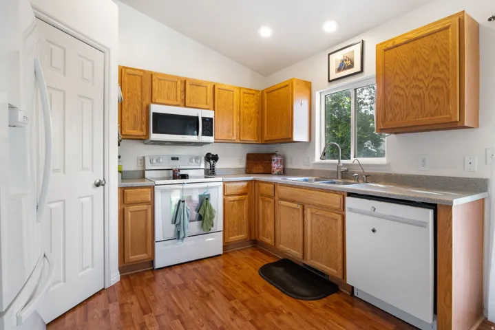 Kitchen featuring laminate flooring, wood cabinetry, white appliances, a stainless steel sink, and recessed lighting