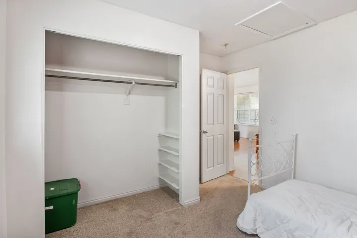 Carpeted room with a built-in closet featuring a hanging rod and shelving