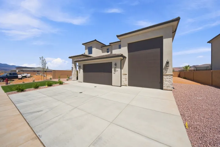 Contemporary stucco exterior with stone accents, two-car garage, concrete driveway, and low-maintenance landscaping