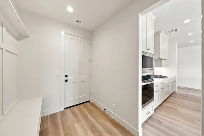 Built-in bench with wall paneling, wood-finish flooring, recessed lighting, and a modern two-panel door