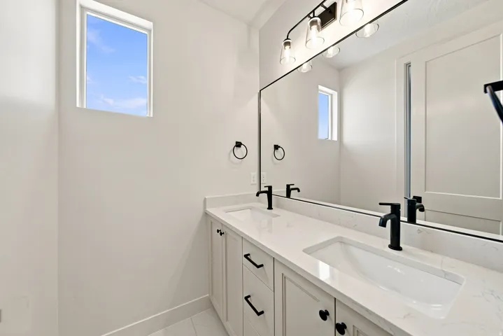 Dual vanity with integrated sinks, stone countertops, matte black fixtures, and a wide mirror