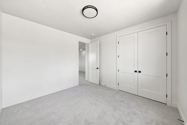 Wall-to-wall carpeting, bright white walls, flush-mount ceiling light, and white paneled doors with black hardware