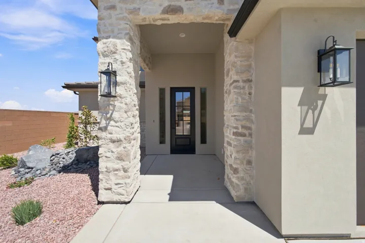 Stone façade entry with a prominent black-framed glass door, recessed lighting, and wall-mounted exterior lanterns