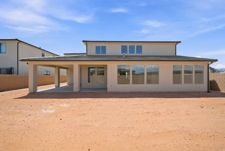 Expansive backyard space with stucco exterior, covered patio, multiple large windows, and a block wall perimeter