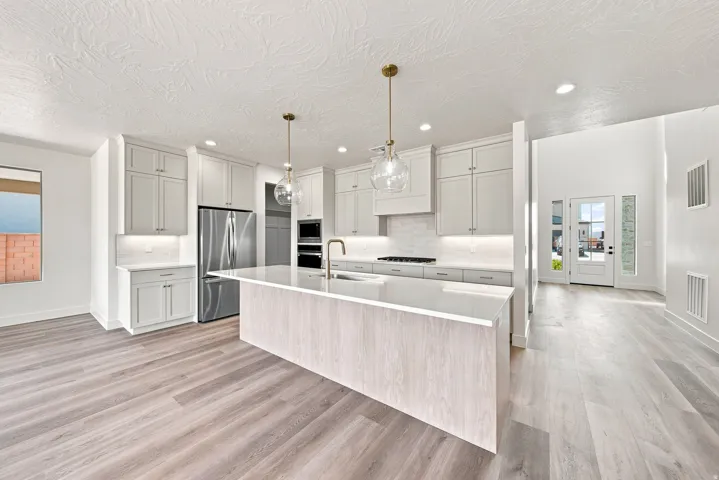 Kitchen featuring wood-finish flooring, an expansive island with a countertop, stainless steel appliances, and white cabinetry