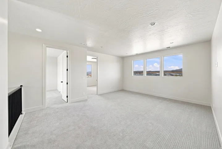 Light gray carpet flooring, white walls, three windows with natural scenery, recessed lighting, and a black metal railing